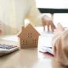 Twee mensen overleggen met rekenmachine en houten afbeelding van een huis