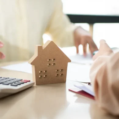 Twee mensen overleggen met rekenmachine en houten afbeelding van een huis