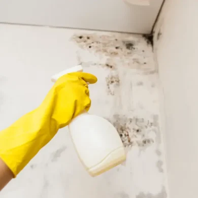 schimmel plek in hoek wordt bespoten door hand in gele handschoen